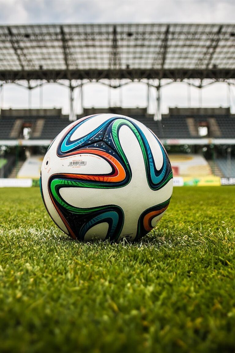 A vibrant soccer ball rests on a lush green field inside an empty stadium, capturing the essence of sports.